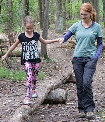 Adult holds girl's hand as she walks over an obstacle in the kid Marsh Mucker course