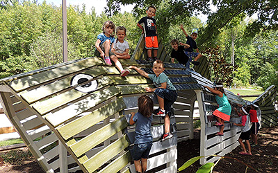 Children climbing on wood play set shaped like a fish